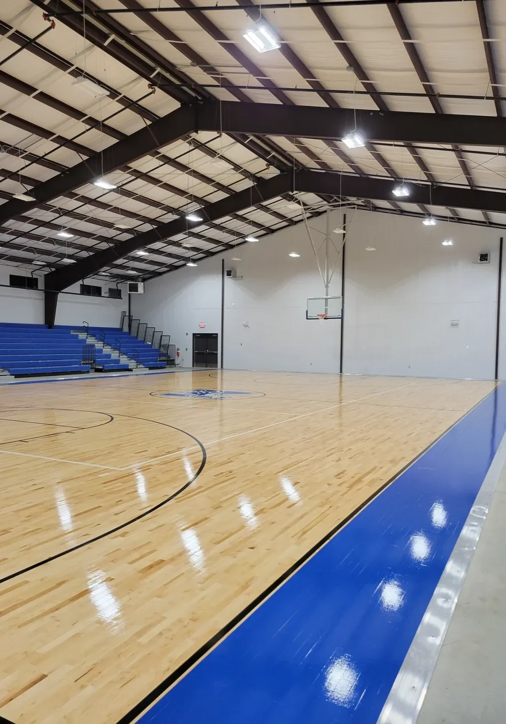 Empty indoor gymnasium with polished wooden floor and blue seating.